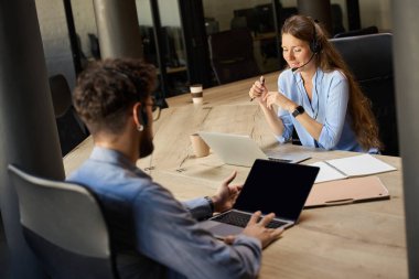 Young caucasian call center operators watching on laptops at desk in coworking office. Concept of teamwork