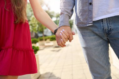 Cropped image of couple holding hands while walking on city pavement in warm summer day. Concept of romantic relationship and date