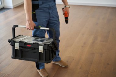 Cropped image of male worker or engineer with blueprint and drill in new modern comfortable townhouse before repair