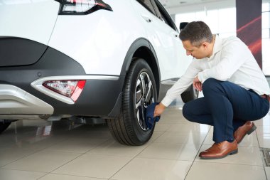 Male in office clothes wipes the wheels of a car, he works in a car dealership