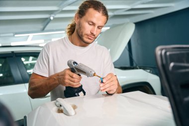 Process of using straightening gadgets in auto repair shop, man repairing white car