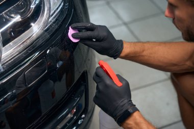 Man is detailing a black car, he applies special clay