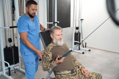 Man performs muscle stretching exercises under the guidance of an experienced trainer, he uses a special machine