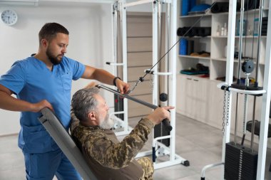 Experienced physiotherapist works with a patient in the gym, a specialist uses a special simulator