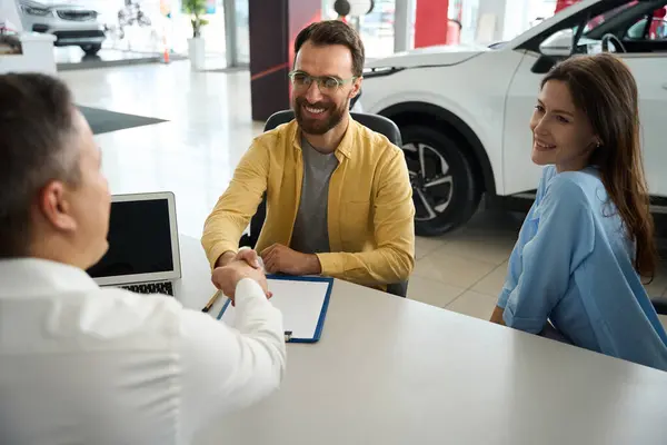 Couple communicates with a consultant in the office area of a car dealership, the men greet each other
