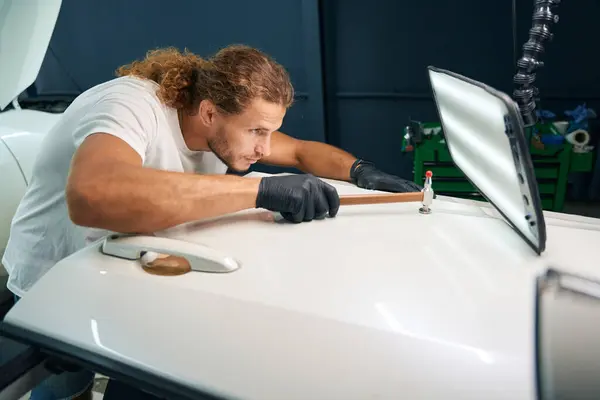 Man levels out dents in the body of a white car, he uses a special straightening tool
