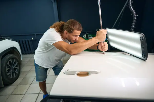 Master uses a special tool to level out body dents, a man straightens a white car