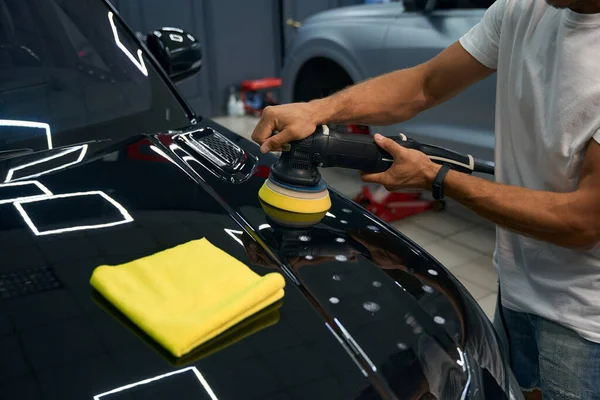 Detailing a car in a car repair shop, the master polishes the hood with a grinder and a soft napkin