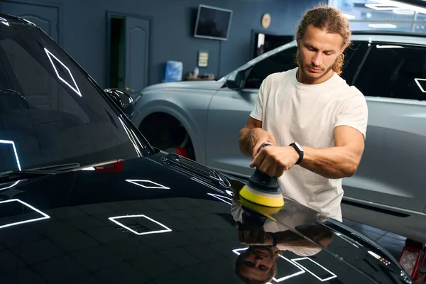 Professional polishes the body of a black car, he uses a special device