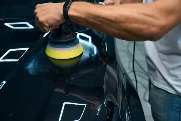 Detailing a modern car in a car repair shop, the master has muscular arms