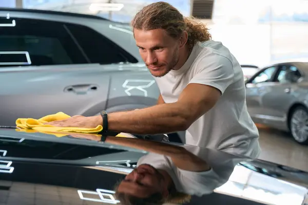 Long-haired guy uses a soft cloth to polish the hood, the guy has muscular arms
