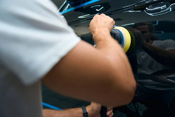 Master with muscular arms polishes car doors with a grinder, a guy works in a car repair shop