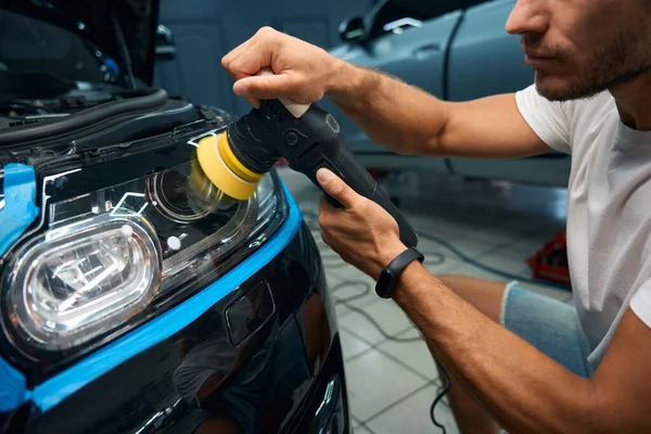 Man in a car repair shop cleans car headlights, he uses a modern device