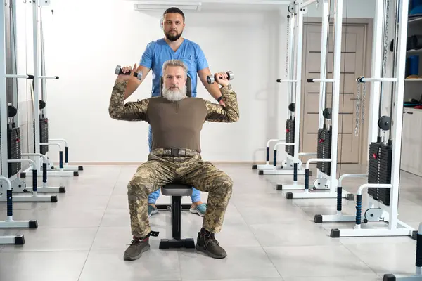 Military man works out in the gym at a rehabilitation center, an experienced physiotherapist works with him