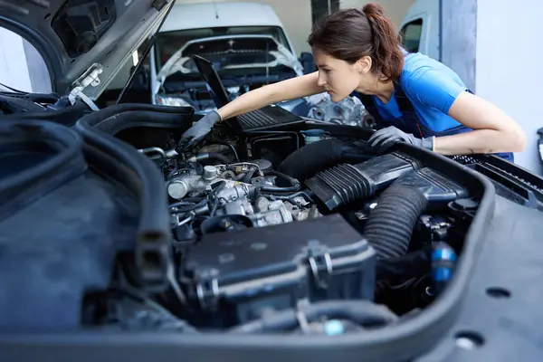 Woman mechanic repairs a car engine, she uses a special tool