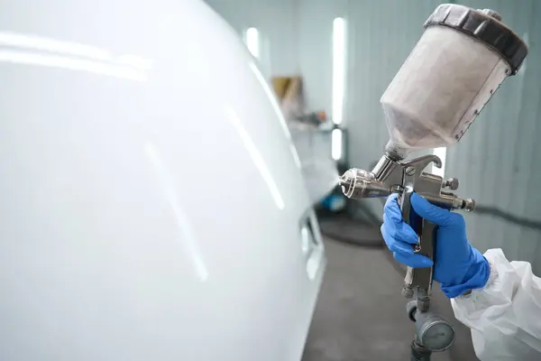 Process of painting a car with a painting apparatus, a man works in protective equipment