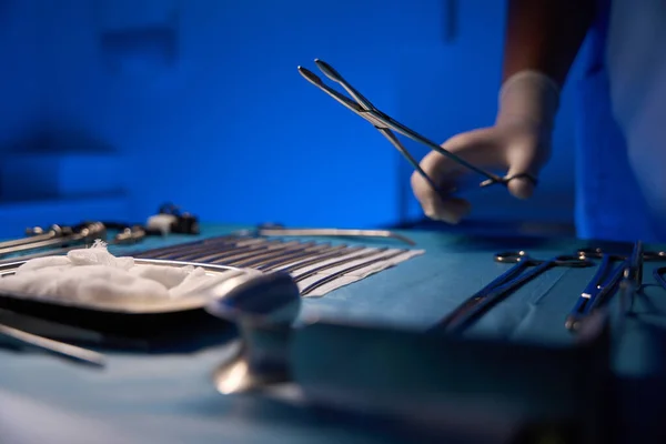 Close up of partial doctor hand taking scalpel from table with medical equipment before surgery in clinic