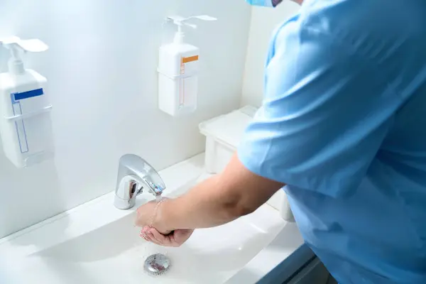 Partial image of male doctor washing hands with water in sink before surgery in clinic. Medical hygiene
