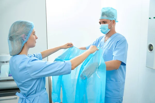 Female Nurse Helping Male Doctor Put Medical Gown Looking Each — Stock Photo, Image