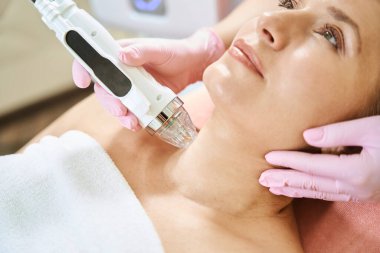 Bulanık güzellik salonunda, IPL fotorejuvenation cihazıyla boyun derisinin mikronedle kaldırılmasını yapan kırpılmış kadın kozmetolojist. Vücut bakımı ve gençleştirme