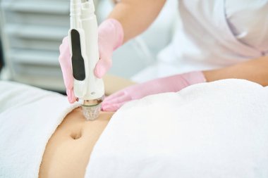 Bulanık güzellik salonundaki IPL fotorejuvenation cihazıyla göbek derisini mikronedle kaldıran kadın kozmetolojistin kesilmiş görüntüsü. Vücut bakımı ve gençleştirme kavramı