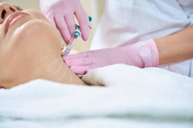 Bulanık güzellik salonunda kadın kozmetik uzmanının, yetişkin kadın şırıngası ile boyun güzelliği enjeksiyonu yaparken kısmi görüntüsü. Vücut bakımı, kaldırma ve gençleştirme