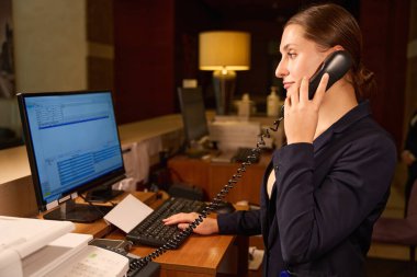 Resepsiyonda beklerken telefonla konuşan ve bilgisayarda bir şeyler yazan kadın yöneticinin yan görüntüsü.