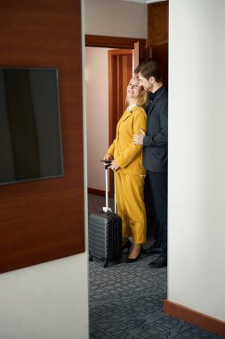 Gülümseyen kadın otel odasında erkek arkadaşının yanında duruyor.