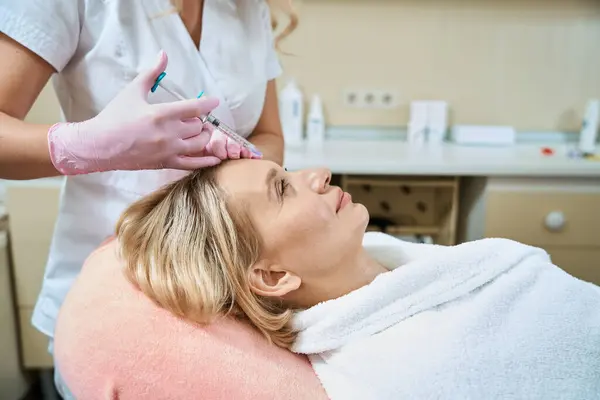 局部女性美容师在模糊美容院用成年高加索妇女浴衣注射器进行面部美容术注射的侧视图 面部皮肤护理 整容及更新 — 图库照片