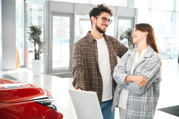 購入する自動車を選択するディーラーに立ってサロンで車を購入する陽気な男と女性 — ストック写真