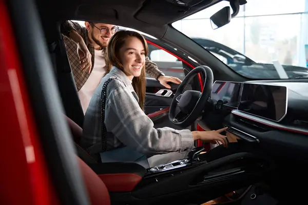 Woman and man choosing model of car in dealership testing modern model for buying