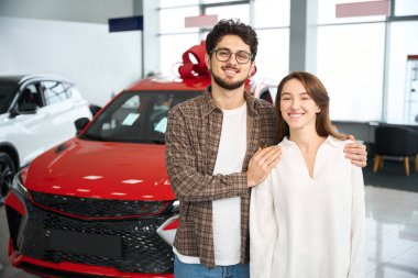 Güzelim genç çift, galeride yeni bir arabada duruyor. Satın almak için araba seçiyorlar.
