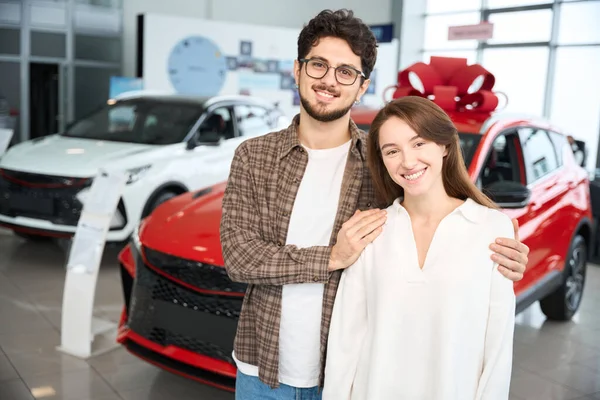 Cheerful Man Hugging Woman While Standing Dealership New Red Car — Stock Photo, Image