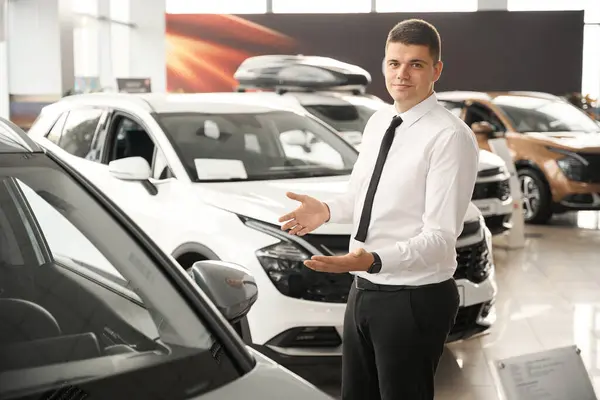 Confident auto salon manager offering new automobile for customers in modern dealership