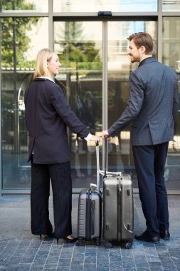 Genç bir adam ve bir kadın otelin girişinde el çantasıyla birbirlerinin önünde duruyorlar.