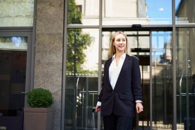 Modern otelin yakınında taksi bekleyen, elinde bavuluyla neşeli bir bayanın yakın çekimini yapın.