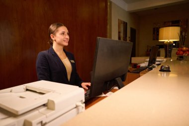 Otelin resepsiyonunda bilgisayarın önünde duran neşeli kadın resepsiyonist.