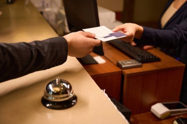 Close up picture of man hand getting keycard in paper envelope from hand of female administrator at reception desk clipart