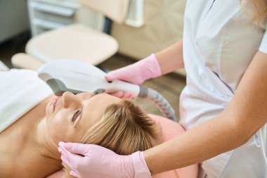 Kısmi kadın güzellik uzmanı bulanık güzellik salonundaki yetişkin beyaz bir kadının IPL fotorejuvenation cihazıyla estetik ameliyat yapıyor. Yüz bakımı ve gençleştirme kavramı