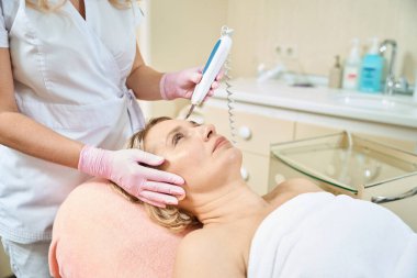 Bulanık güzellik salonundaki yetişkin beyaz bir kadının IPL fotorejuvenation cihazıyla yüz derisini ultrasonik olarak temizliyor. Yüz bakımı ve gençleştirme kavramı