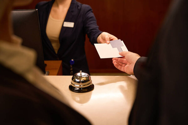 Close up photo of receptionist hand giving plastic key card in paper holder to guest hand