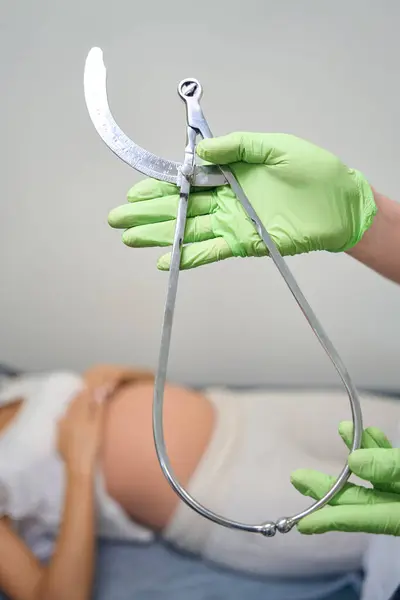 妇科医师手握产科骨盆计数器 在临床的医疗沙发上 有模糊孕妇背景的选择性聚焦 怀孕检查的概念 — 图库照片