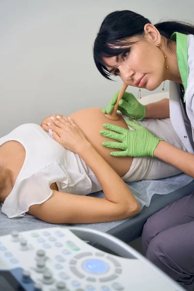 欧洲女性妇科医生在临床上专心致志地倾听部分孕妇的腹部 怀孕检查的概念 — 图库照片