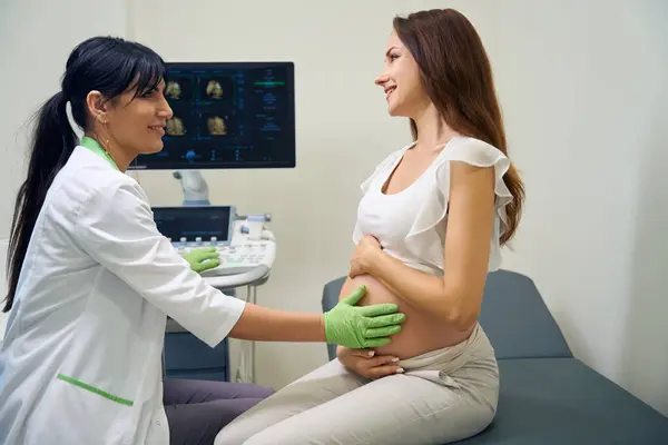 欧洲成年妇科医生在临床上检查年轻高加索孕妇腹部的侧视 怀孕检查的概念 — 图库照片