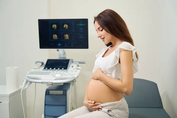 Young Caucasian Pregnant Woman Sitting Medical Couch Looking Her Belly — Stock Photo, Image