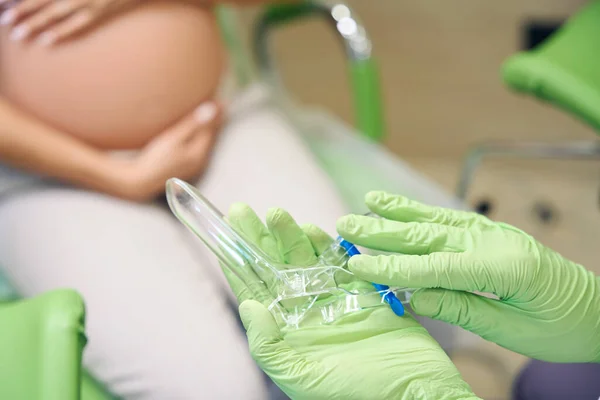 女性の婦人科医のラテックス手袋を着用した手の排気管を持つ婦人科鏡は クリニックの露出した妊婦の近くにあります 妊娠検査の概念 — ストック写真
