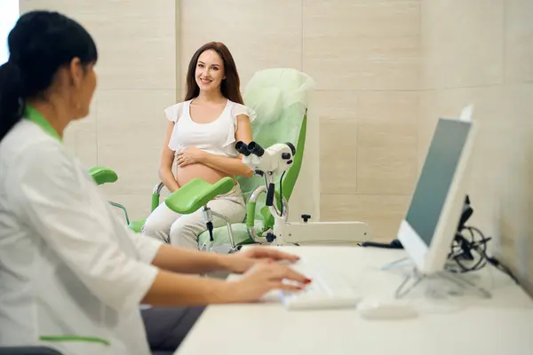 在检查年轻的 面带微笑的高加索孕妇时 女妇科医生在电脑上打字 她们在诊所里互相望着对方 怀孕检查的概念 — 图库照片