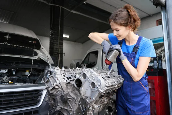 Young woman master repairs a car engine, she uses a special tool