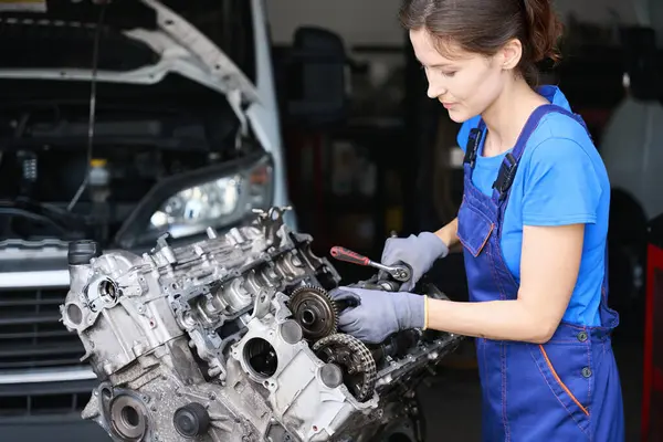 Female auto mechanic is repairing a large auto part in an auto repair shop, she is wearing a blue uniform