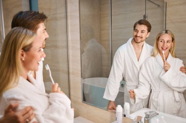 Neşeli eşler banyoda sabah rutinlerini yapıyorlar, rahat Terry cüppeli bir çift.